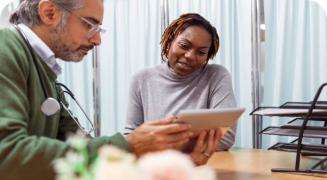 Doctor sitting as desk with woman looking at tablet